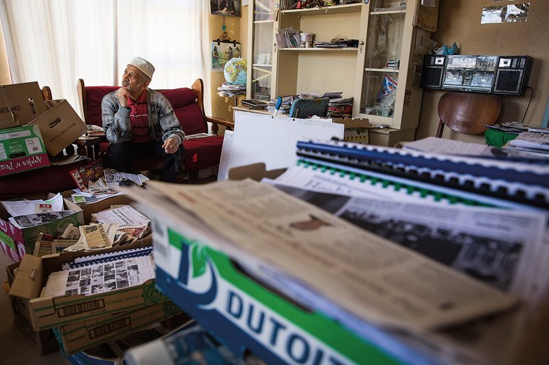 Local historian and archivist Ebraheim Manuel sits in his living room surrounded by newspaper articles and photos he has collected relating to Cape Malay history. The 71-year-old has lived through much of that history&mdash;including both apartheid and, as a teenager, the Group Areas Act that forcibly relocated families.