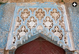 Seven medallions, framed by floral and shell motifs, decorate a carved and painted panel above a doorway. The medallions on the panels flanking it repeat “[there is] no victor but God.”