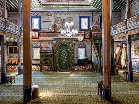 Beghleti mosque's stunning interior woodwork and colorful ornamentation stand in sharp contrast to the corrugated- metal exterior of it and other wooden mosques in the region.