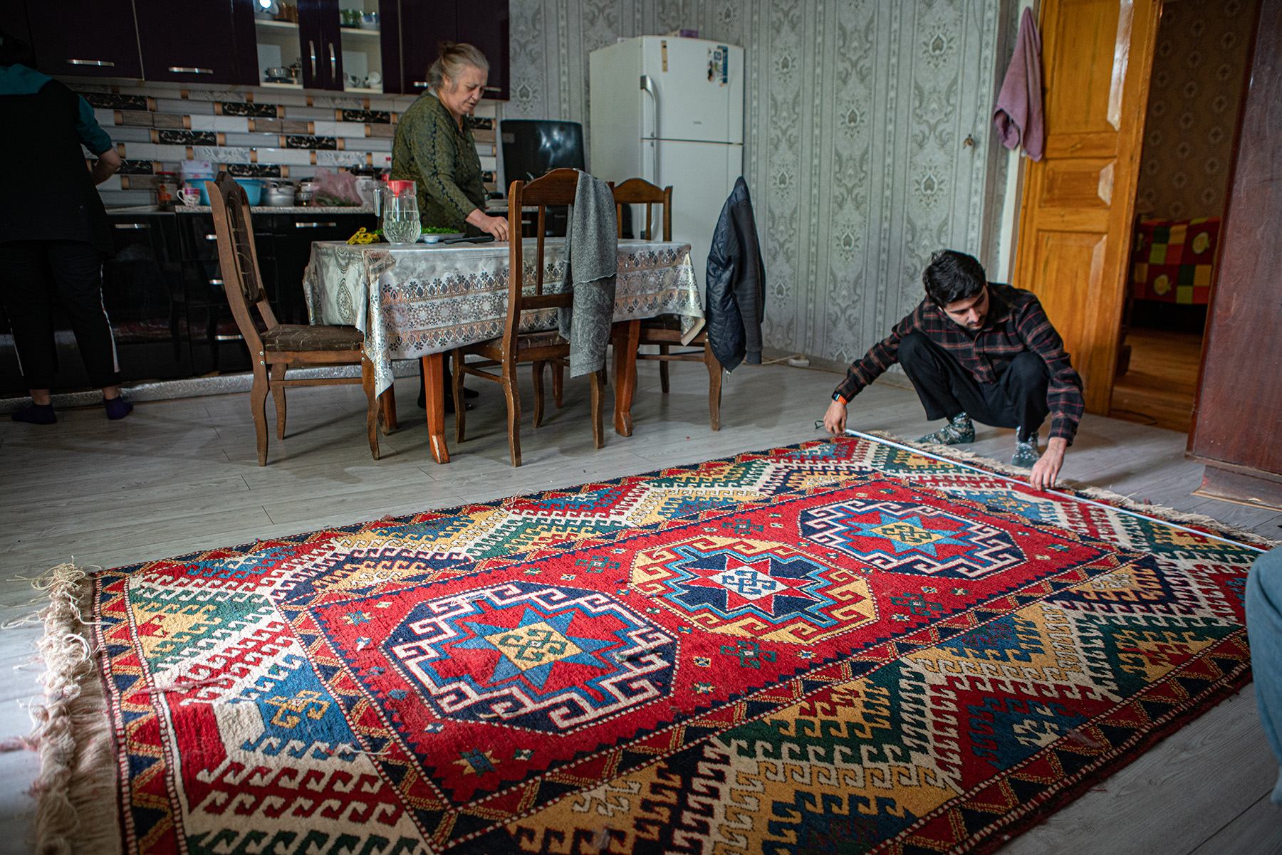 reWoven coordinator Zaur Khalilov measures the final dimensions of a recently completed rug woven by Suraya Memisova at her home.