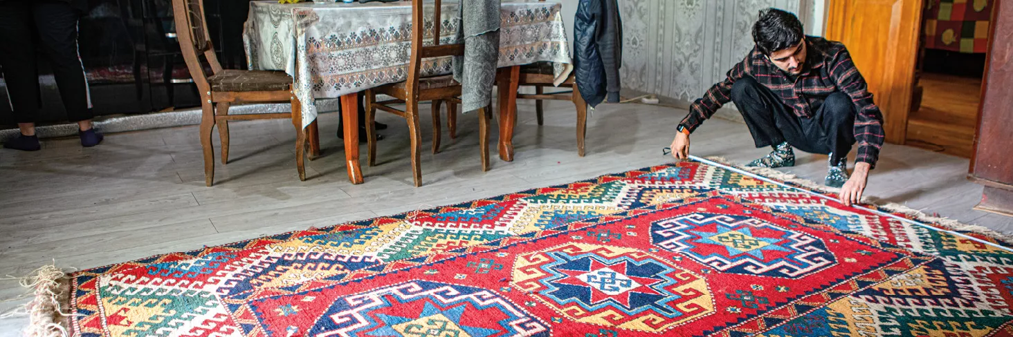 reWoven coordinator Zaur Khalilov measures the final dimensions of a recently completed rug woven by Suraya Memisova at her home.