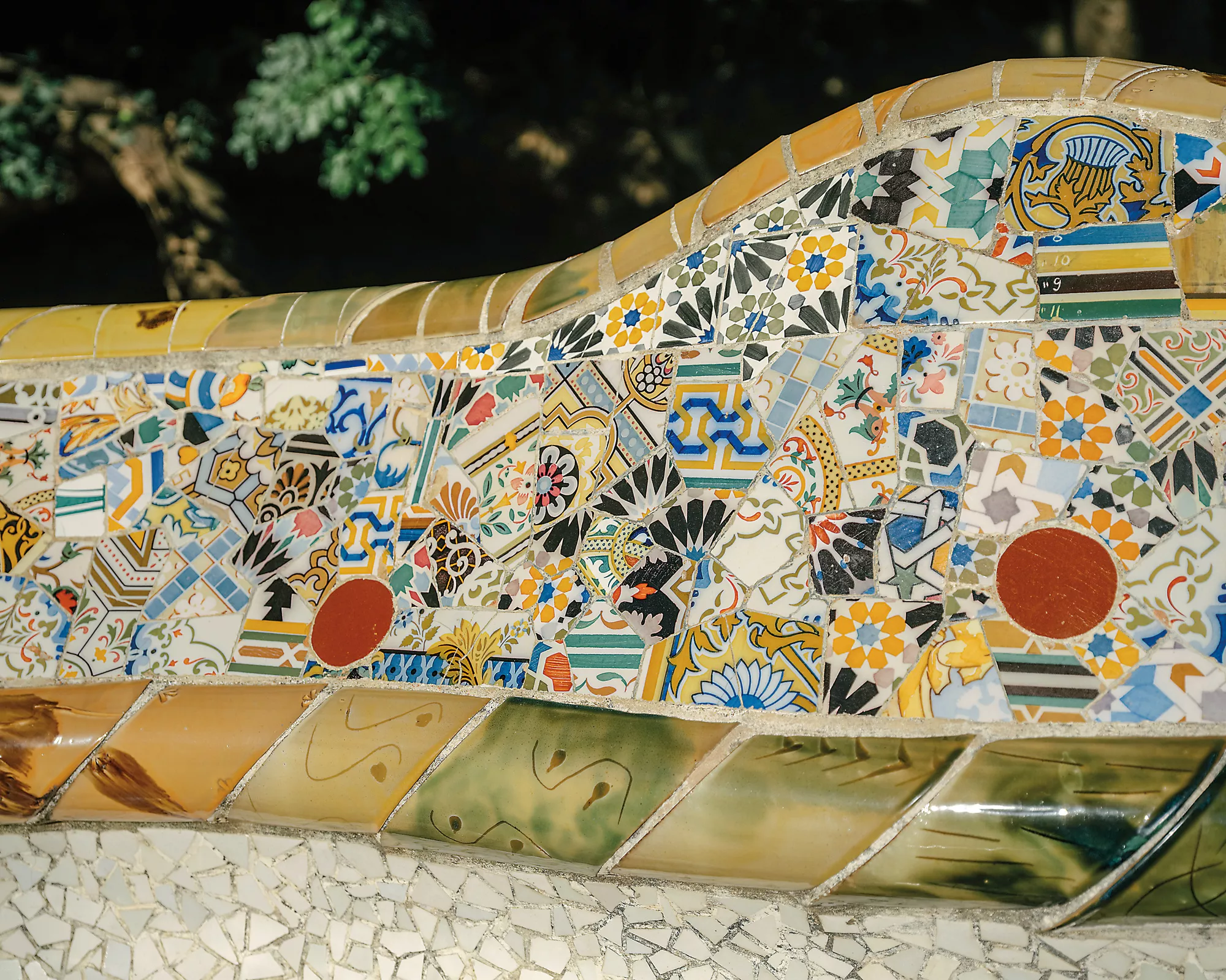 Gaudí covered Park Güell's serpentine bench with trencadís, arranging irregular pieces of broken ceramic into colorful patterns. The technique illustrates how Gaudí transformed artistic influences rather than simply reproducing them.