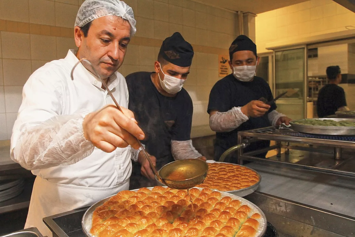 The final touch of baklava-making is syrup, heated to precisely 108&deg; centigrade (226&deg; F) and poured onto baklava just out of the oven, here by head chef Coşkun Koçak. "Only in Gaziantep is the syrup added hot to freshly-baked baklava," says Hösükoǧlu. "This hot-to-hot is what gives Gaziantep baklava its very special flavor.&rdquo;