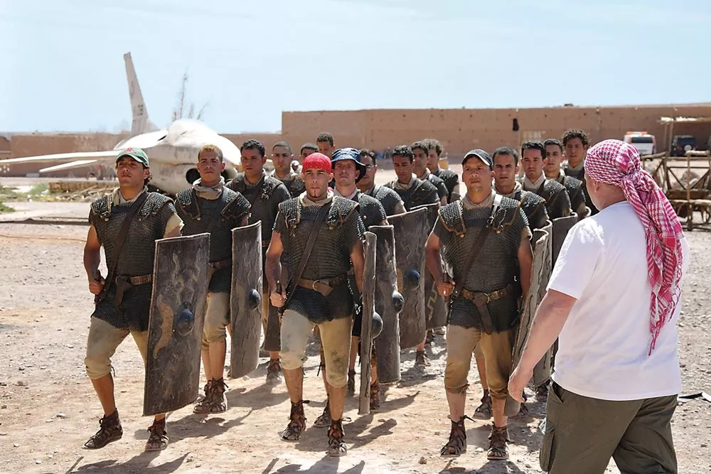 Seeming like a clash of centuries, extras costumed as Roman centurions practice marching at Atlas Studios for a scene in the series <i>Ben-Hur</i> while a mock F-16 fighter jet, used in <i>The Jewel of the Nile</i>, stands behind them.
