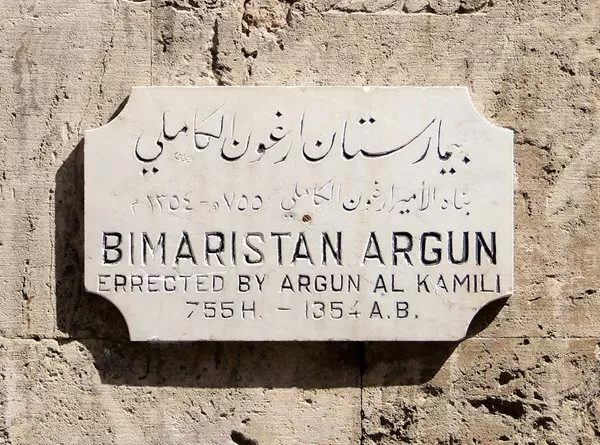 <p>This plaque on the wall of the Bimaristan Arghun in Aleppo, Syria, commemorates its founding by Emir Arghun al-Kamili in the mid-14th century. Care for mental illnesses here included abundant light, fresh air, running water and music.&nbsp;</p>
