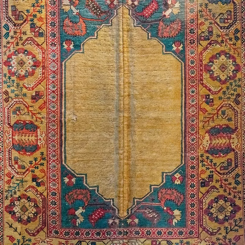 This rug&rsquo;s design started with a traditional <i>mihrab</i> (direction of prayer) plain niche, and added a second one below in mirror-image. Such rugs were made for export to Christian lands, for their dual-niche patterns complied with the Ottoman edict barring Islamic religious imagery from carpets sold to non-Muslims.