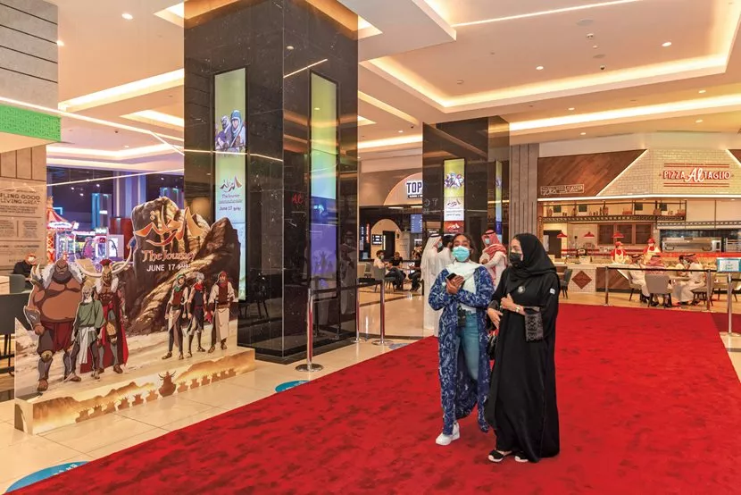 Saudis pass a movie poster for The Journey at Vox Cinemas Riyadh. After the pandemic delayed its release, the film opened in Japan and Saudi Arabia in June 2021 and later elsewhere around the world.