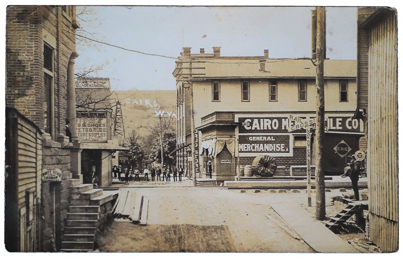Printed in the early 1900s when its population stood below 700, this view of Cairo, West Virginia, shows a road-surfacing crew lined up across the railroad tracks that ran down Main Street. Behind the men stands one of the oil derricks that proliferated then in this part of the state.
