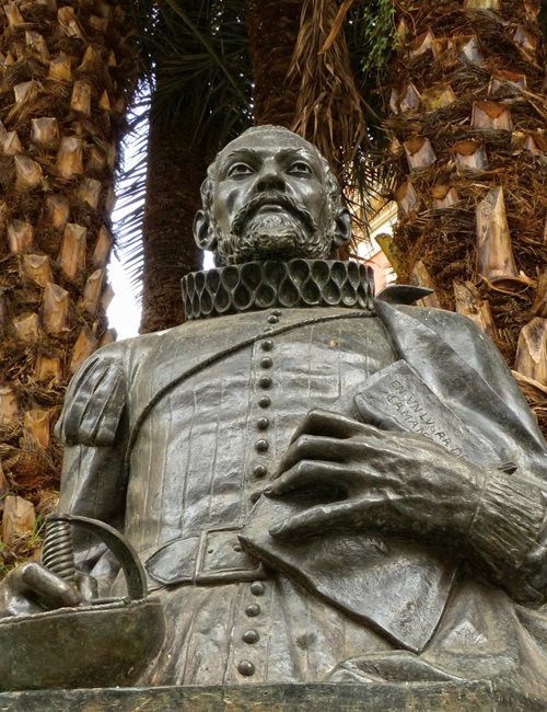 This statue of author Miguel de Cervantes stands near the notorious alley between the former Inquisition prison and the former Royal Jail where it is thought Cervantes, while held there, began composing his manuscript, which he holds inscribed with its famous opening line, “En un lugar de La Mancha” (“Somewhere in La Mancha”).