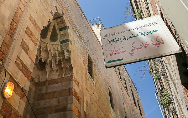 In a narrow street of Old Jerusalem, a sign in Arabic points the way to <i>Takiyah Khaski Sultan</i>, the charitable soup kitchen founded in 1552 by the wife of Ottoman Sultan Suleiman. <b>Below</b>&nbsp;Recipients line up outside the courtyard that with the kitchen, a school and a mosque forms the fully endowed charitable complex.