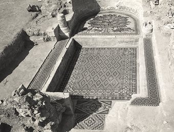 <p>Today, the walls of the diwan have been restored. When it was excavated, as shown in this photo, the room had to be cleared of the rubble of carved plaster that had fallen from the walls and ceiling. This photo also shows the diwan&rsquo;s inner, apsidial platform, with the Tree of Life motif, which appears in full in this calendar&nbsp;in December.</p>
