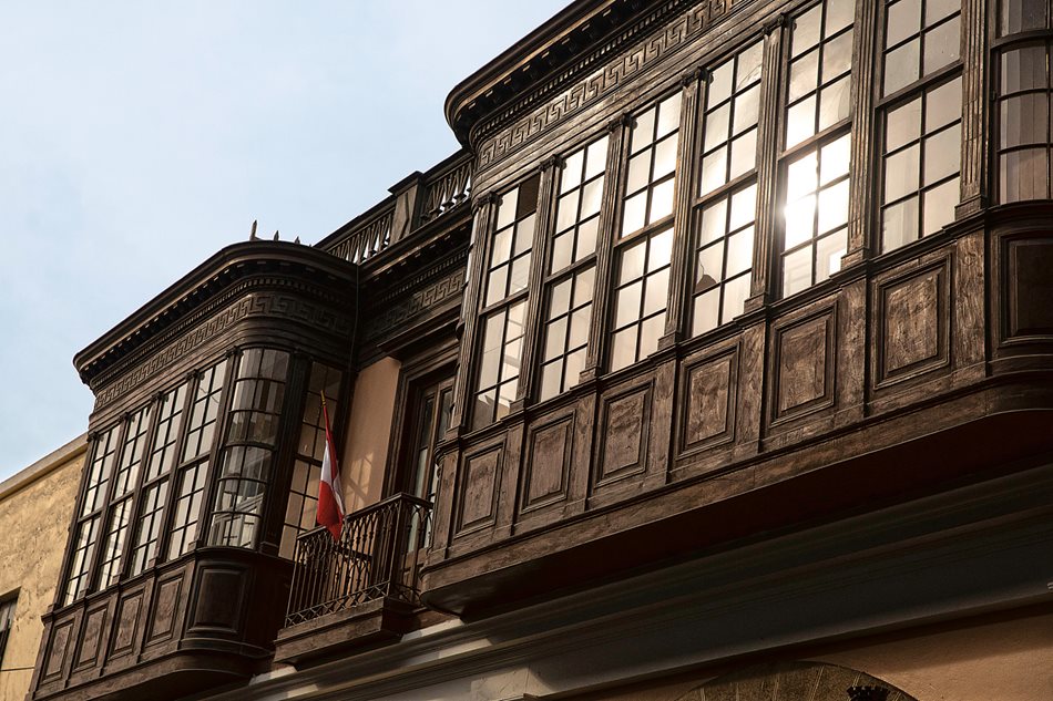 By the 19th and 20th centuries, glass had taken the place of mashrabiya screens, and woodwork on lower walls was simple or elaborate depending on what the owner could afford. Along Jirón Junín, above, two balconies show spare design: ribbed pilasters offer a nod to European neoclassicism, and along the top a winding-pattern band faintly echoes mudéjar influence.