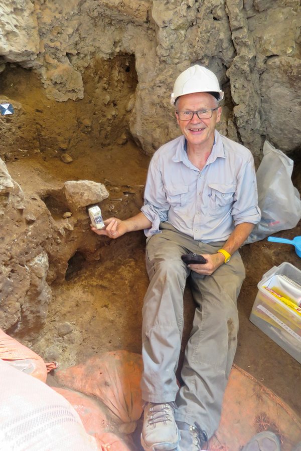 Close to Solecki’s excavation, Barker holds a block of soil that will be analyzed using micromorphology techniques not known in the 1950s. Behind him, Neanderthal bone remains can be seen protruding out of the soil.
