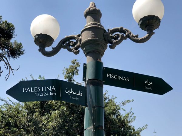 A lamppost gives the direction to local swimming pools and to Palestine, in Spanish and Arabic, in Santiago&rsquo;s barrio Bellavista.