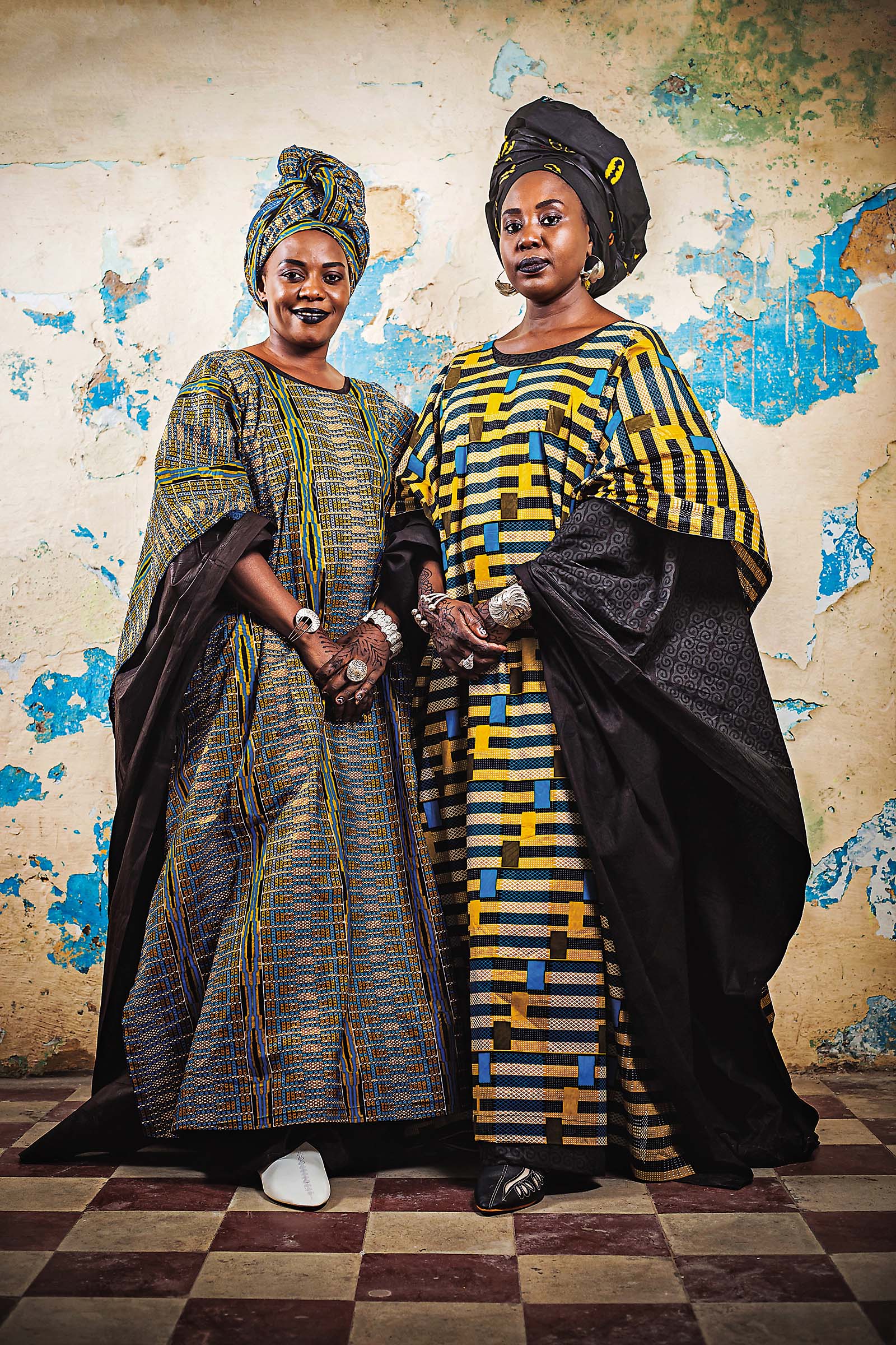 “Duet” comes from the Latin root word duo which means two. The Duet series focuses on double portraits, a tradition in West Africa. I try to create a duality, a resemblance between two people through gestures, clothing, poses, etc. This series includes portraits of relatives, friends and people united by other ties. This particular image is one from a series showing portraits of men and women pridefully posing in front of walls reminiscent of Saint-Louis, Senegal, and its architectural heritage, old buildings steeped in history. At their feet lies a dark checkerboard reminiscent of traditional photo studios.