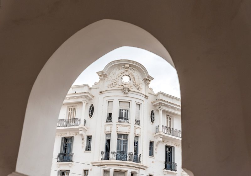 A European baroque-revival building framed by a pointed arch juxtaposes the colonial and local stylistic traditions that give Casablanca both identity and historic tension.