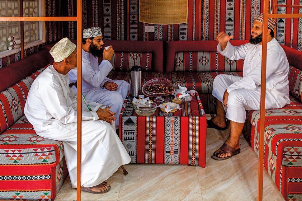 A group of Omani men wearing different colors of kummahs sit chatting at a cafe in a suq at Nizwa, al-Dakhiliyah Region. Predominantly worn around the Indian Ocean, kummahs have taken on a variety of styles and designs introduced across the region, but as many people believe, the kummah remains an Omani innovation.