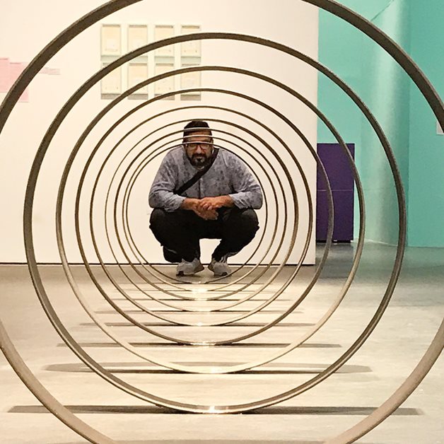 Curator Murtaza Vali with Rayyane Tabet&rsquo;s &ldquo;Steel Rings,&rdquo; 2013, rolled, engraved steel with kilometers, longtitude, latitude and elevation marking locations on the Trans-Arabian Pipeline (Tapline).&nbsp;