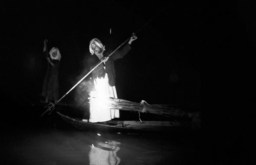 Spearfishing at night requires balancing in a narrow mashuf by the light of a torch of bundled reeds.