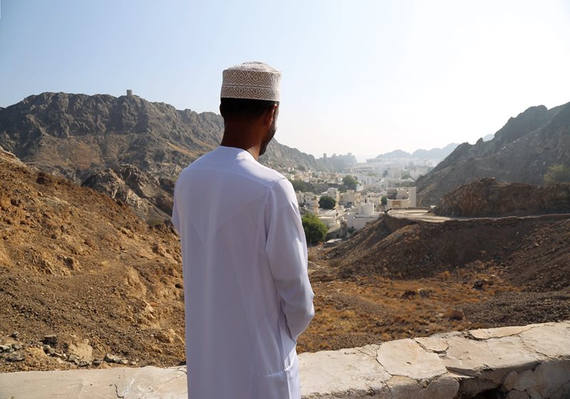 A man wearing a kummah looks across Old Muscat. Kummah is traditionally worn by men in Oman.
