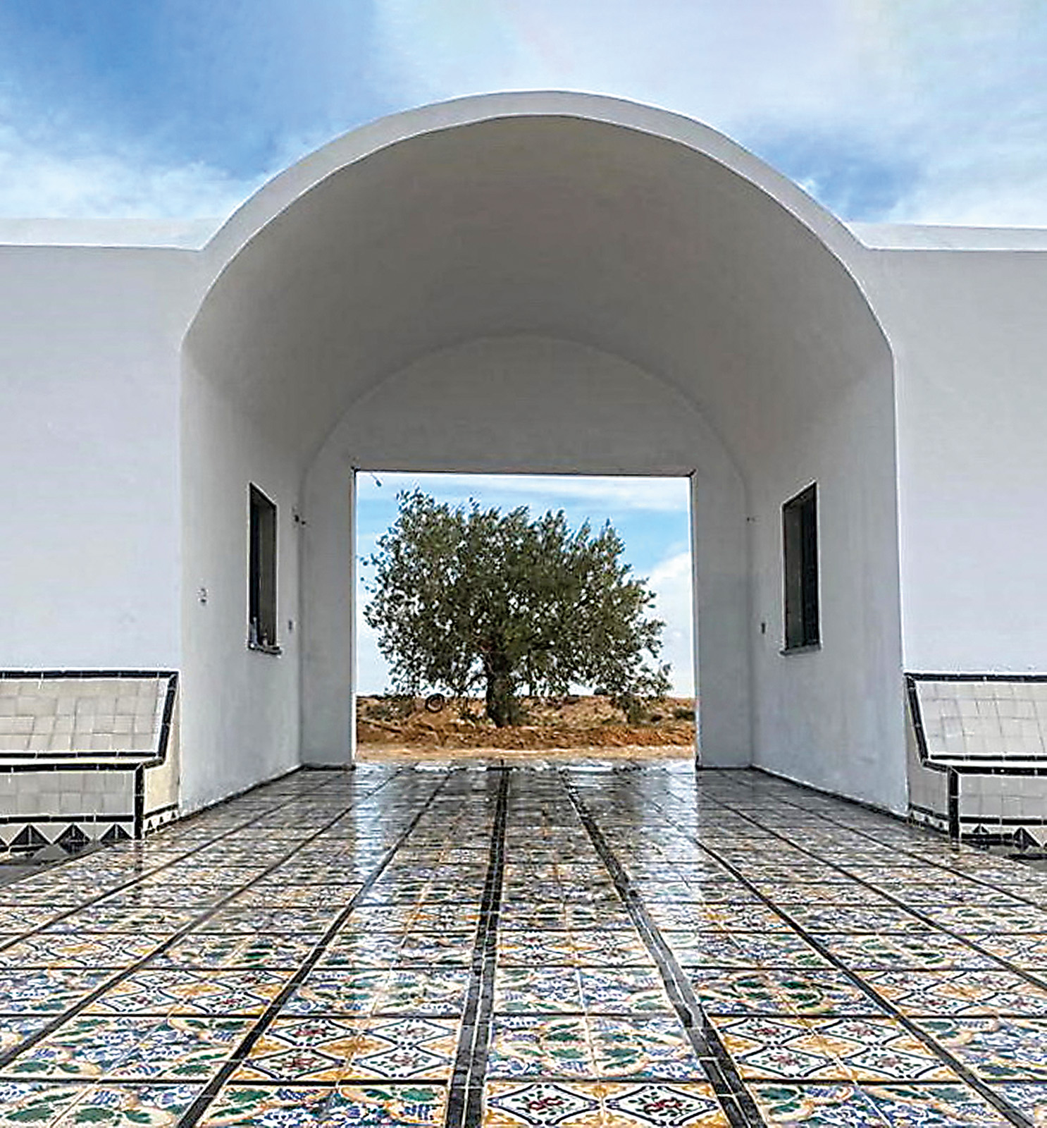 Paths tiled with designs from the renowned Tunisian craft town of Nabeul lead through the cemetery, where a portal frames one of five olive trees that represent the five pillars of Islam. 