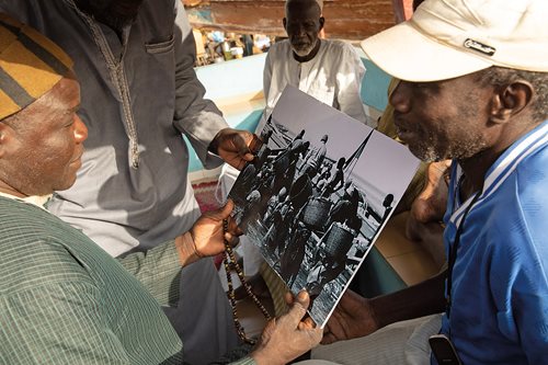 On Mbor beach retired fishermen look over a photo from the 1960s that shows a crew carrying fish off a pirogue in baskets.